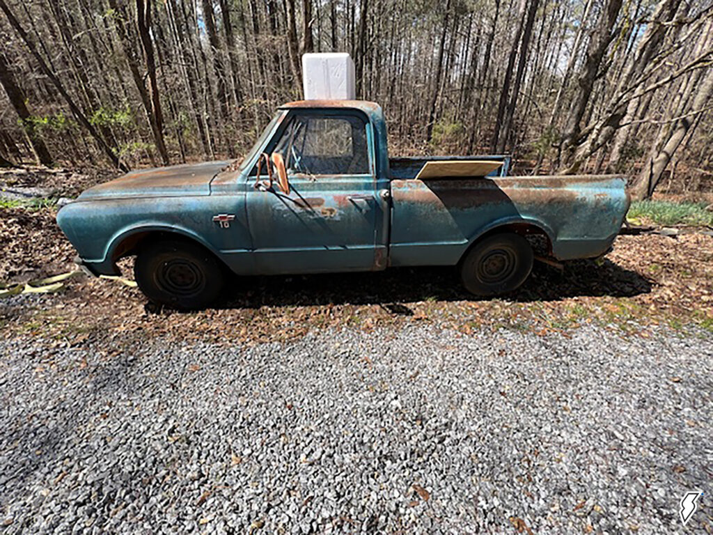 old, rusty Chevy C10 project truck in a gravel lot